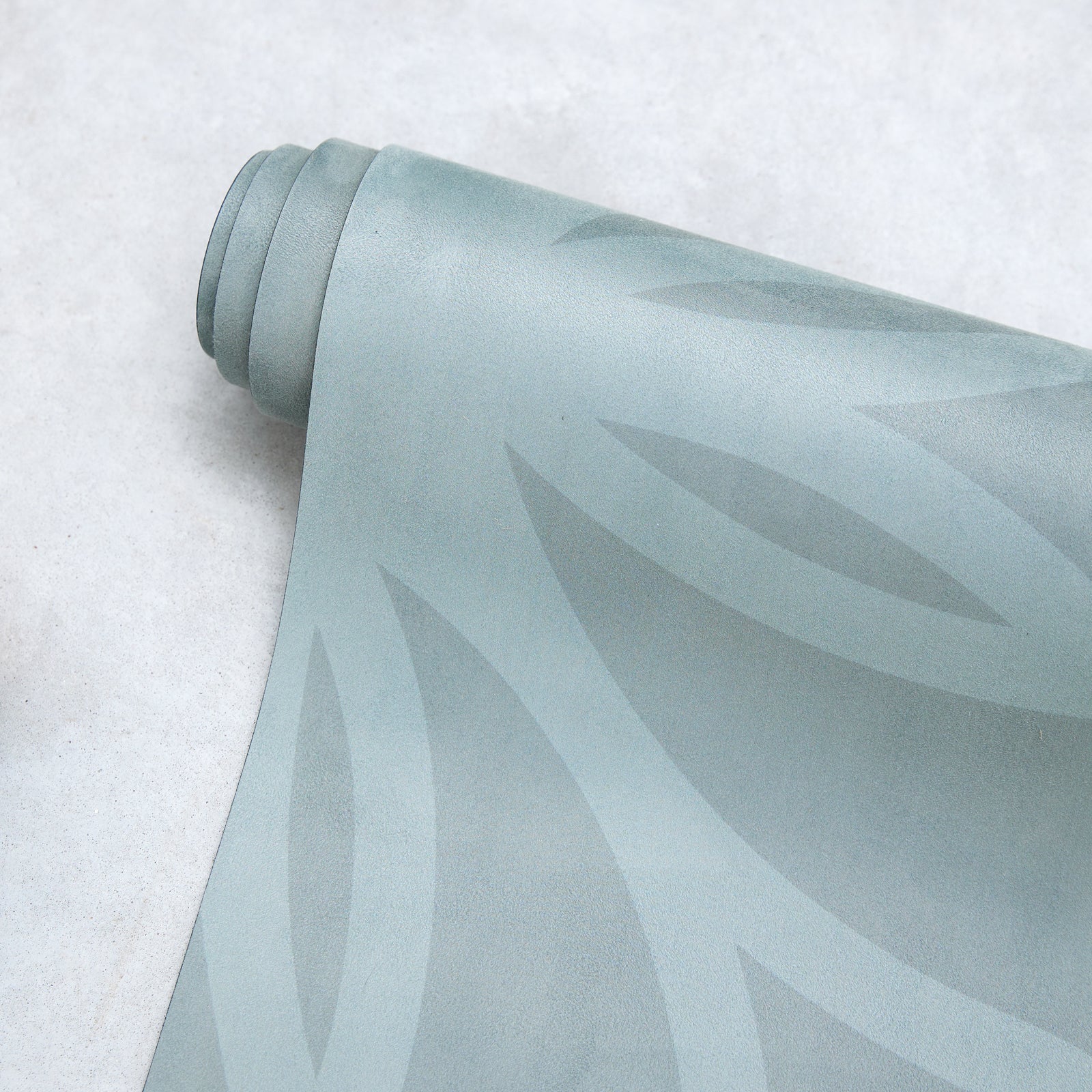 Rolled Anjali Generation eco suede light green yoga mat with leaf pattern on a textured surface