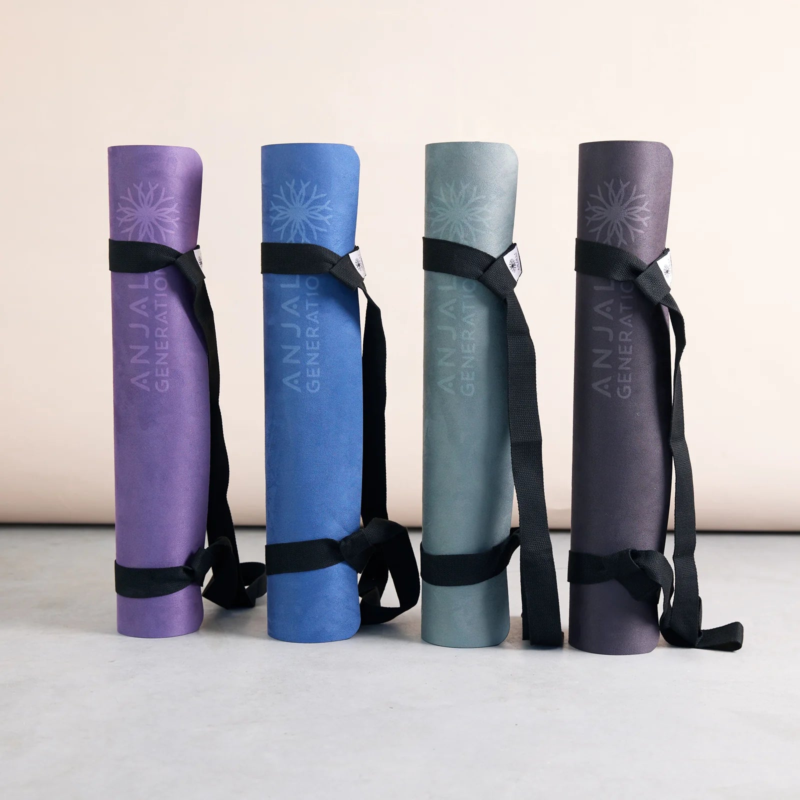 Four Anjali Generation eco suede yoga mats with straps on a light background