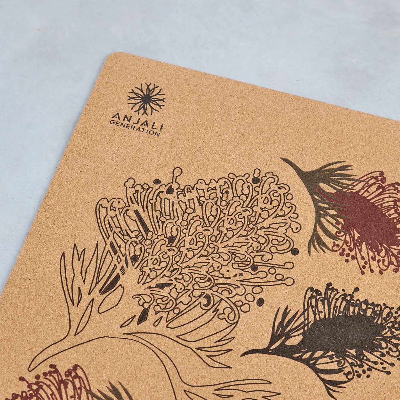 Anjali Generation cork mat with grevillea botanical design and Anjali Generation logo on a light blue background