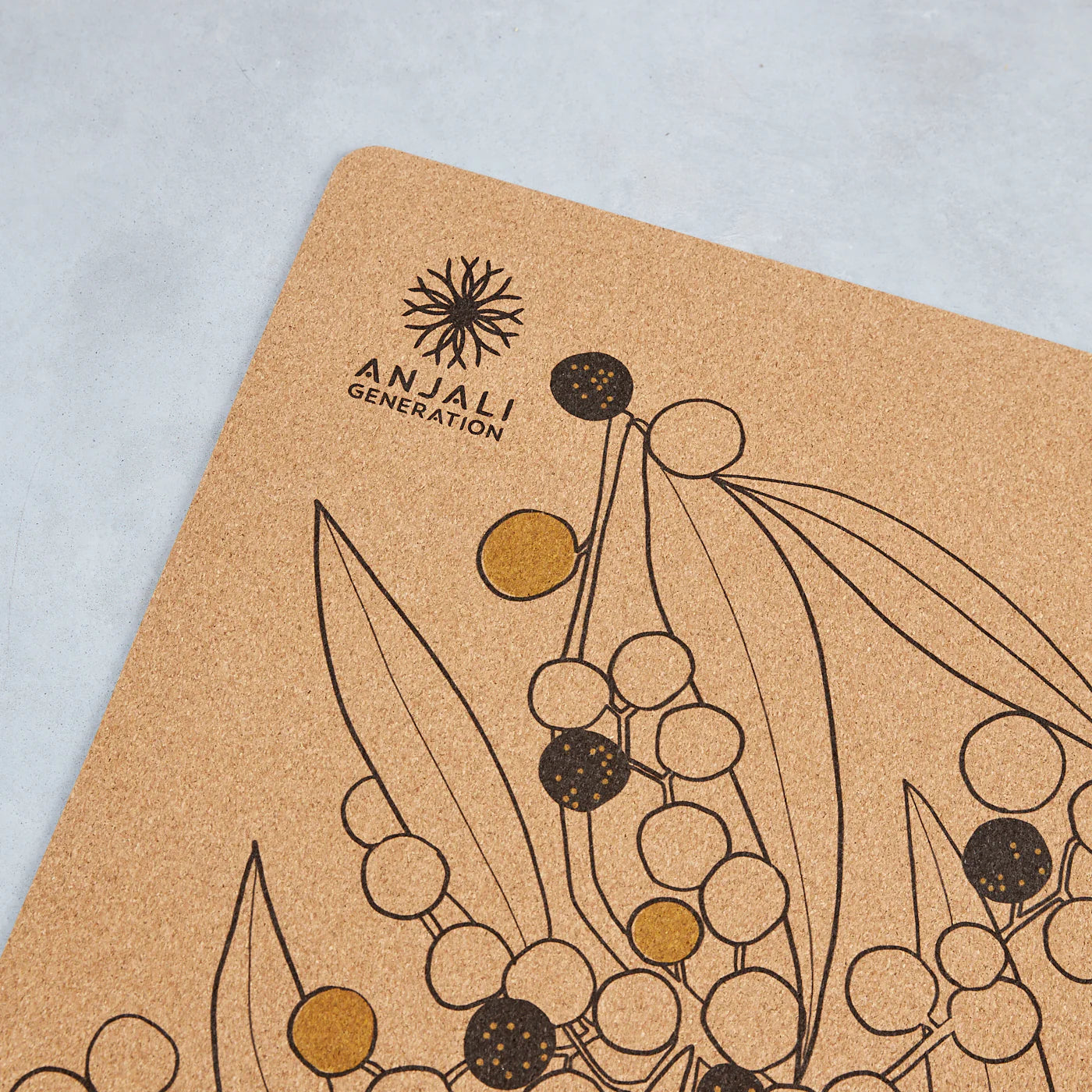 Cork mat with wattle botanical design and Anjali Generation logo on a light blue background
