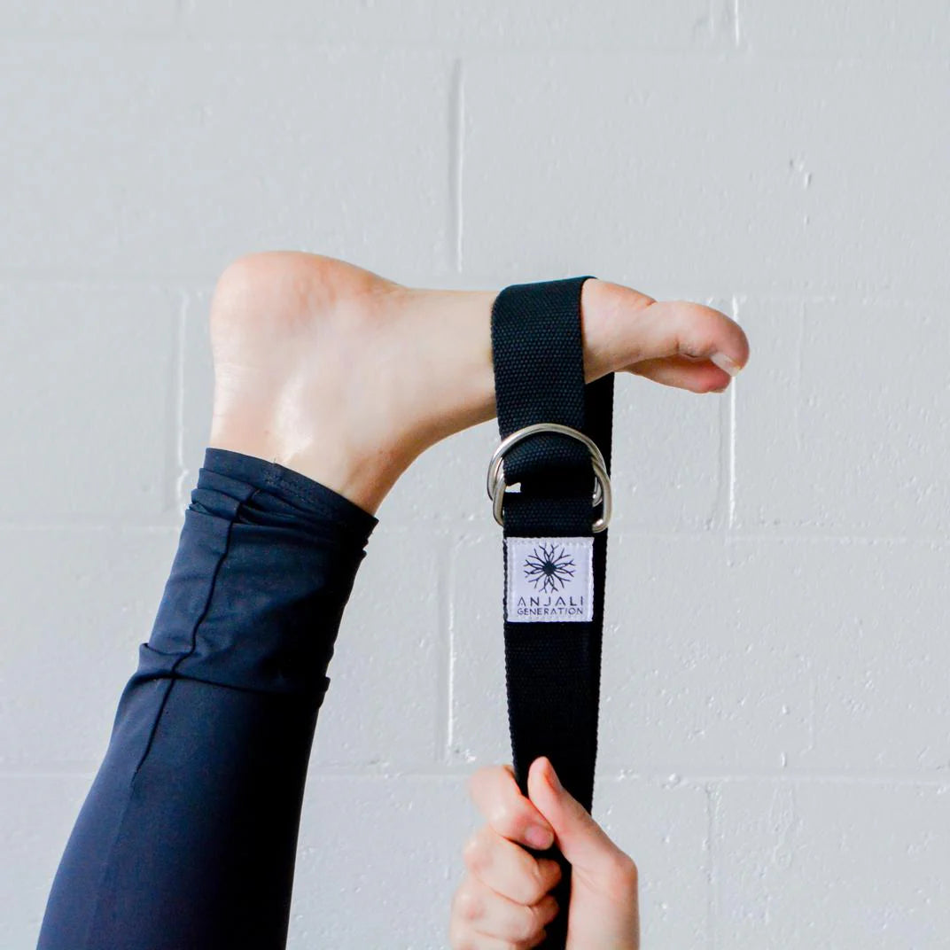 Person using an Anjali Generation black yoga strap with a visible brand logo against a light gray background