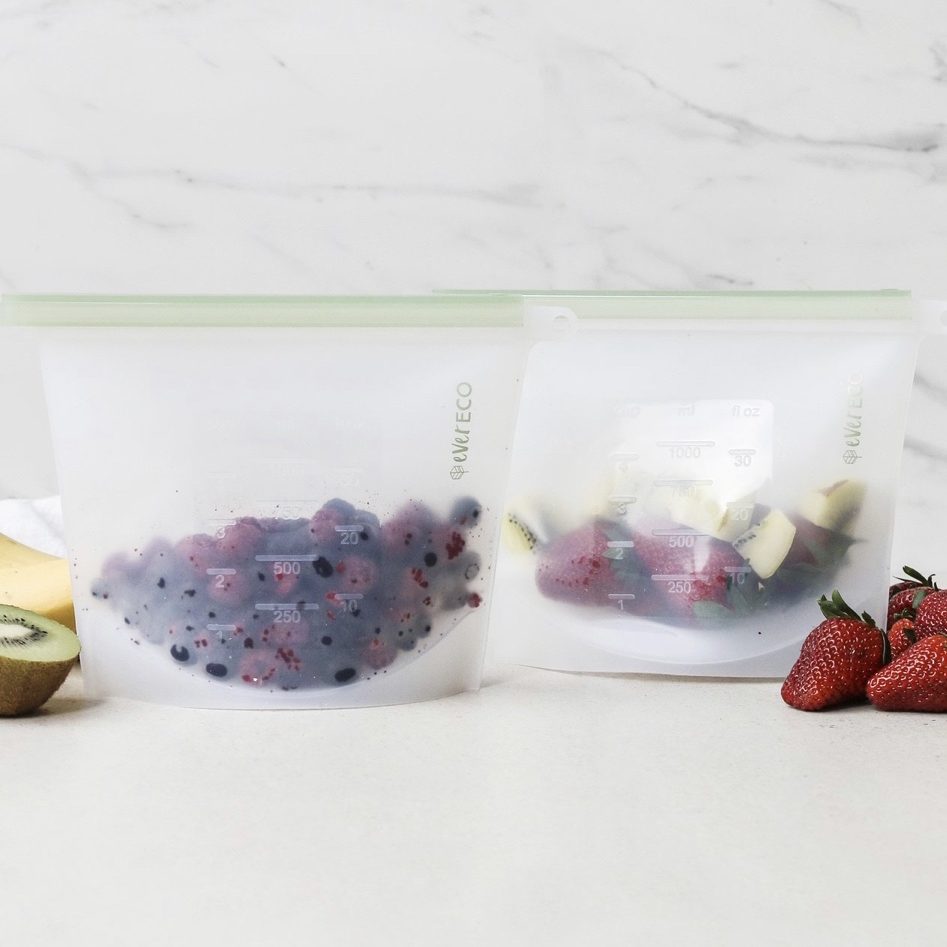 Two Ever Eco reusable silicone food storage bags with fruits and vegetables on a white surface.