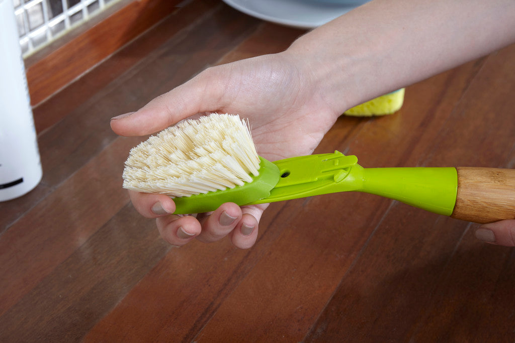 Person holding a Full Circle green and yellow scrubbing brush on a wooden bench.