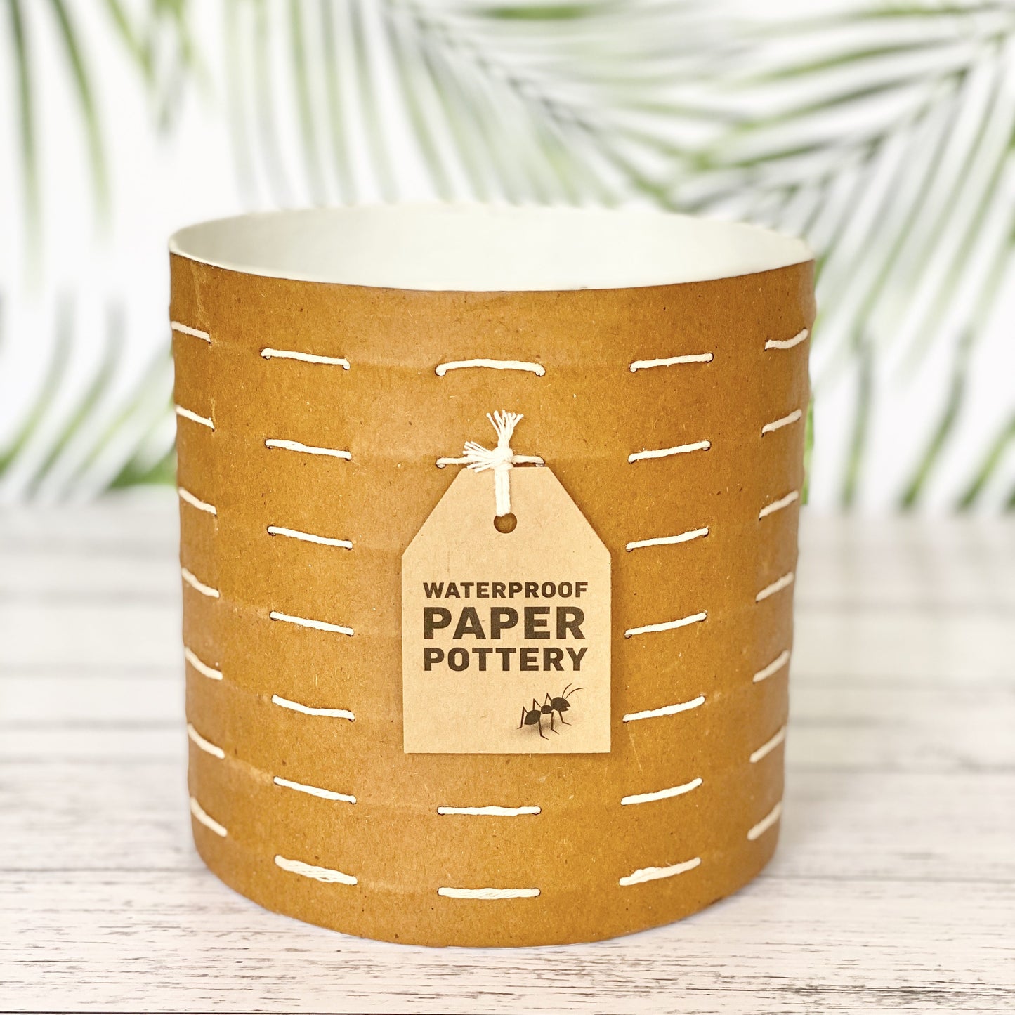 EcoMax paper pot in brown with white stitches with decorative tags on a wooden surface