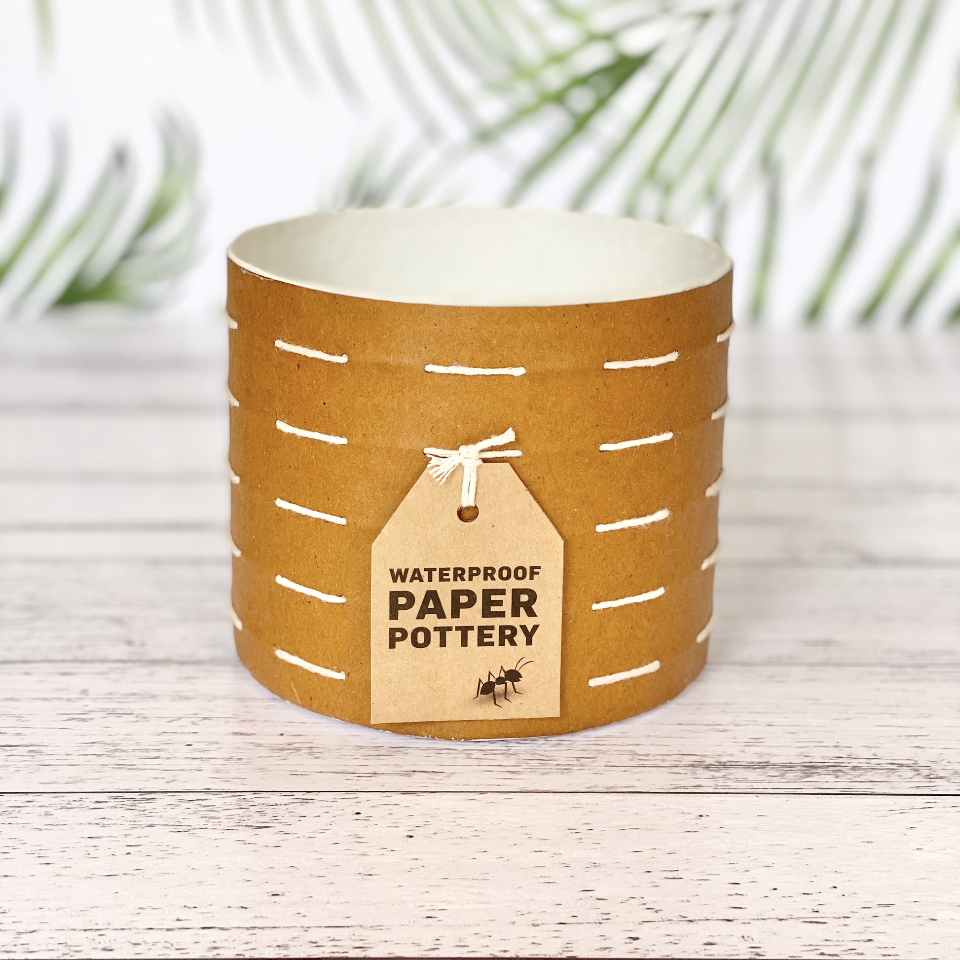 EcoMax paper pot in brown with white stitches with decorative tags on a wooden surface