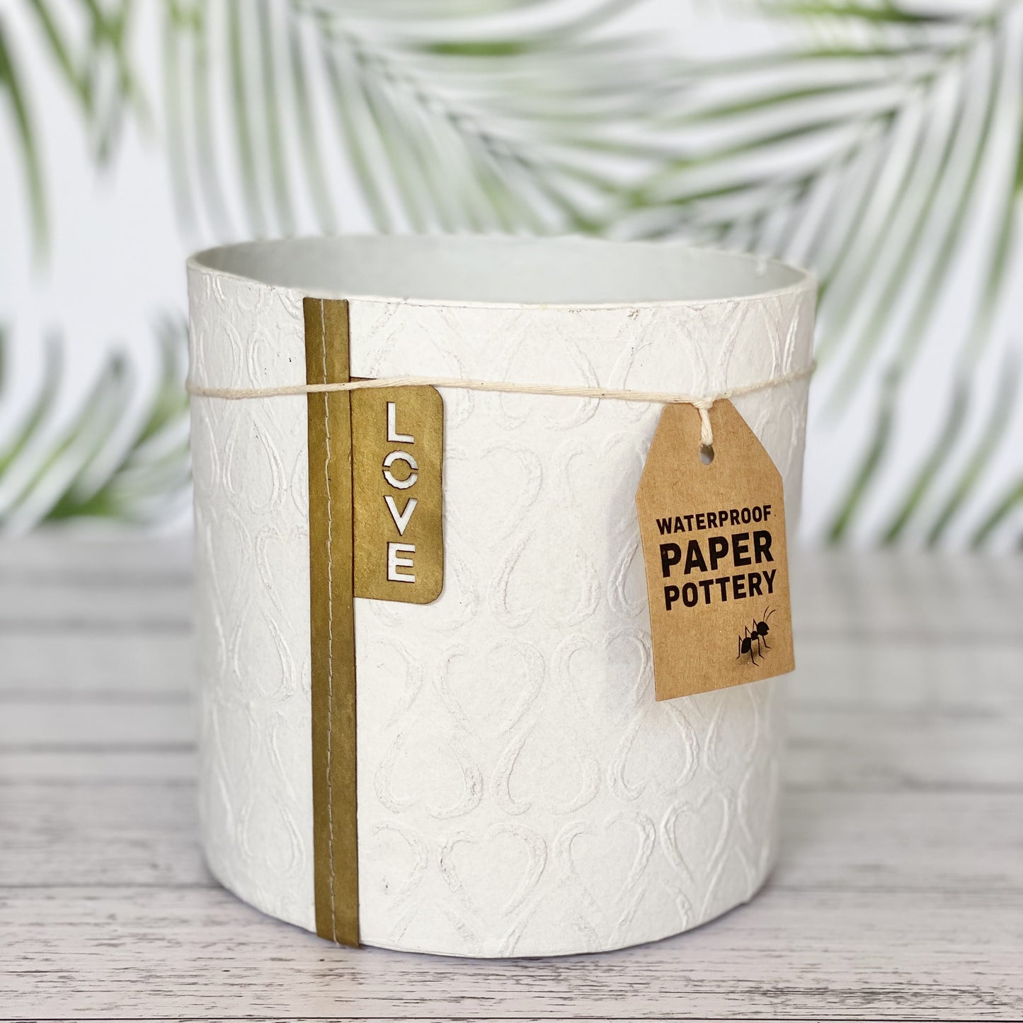 EcoMax paper pot in white with heart pattern with decorative tags on a wooden surface
