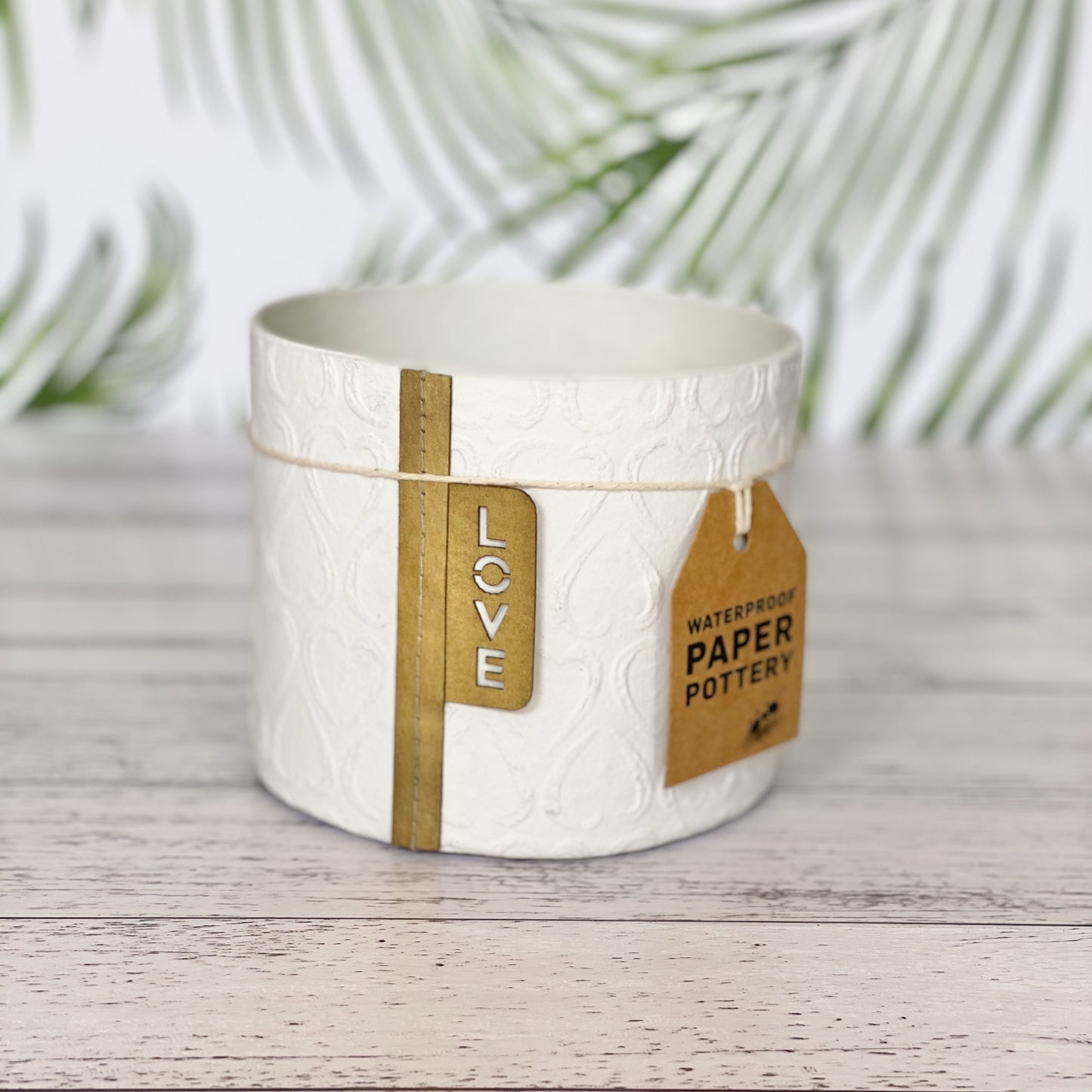 EcoMax paper pot in white with heart pattern with decorative tags on a wooden surface