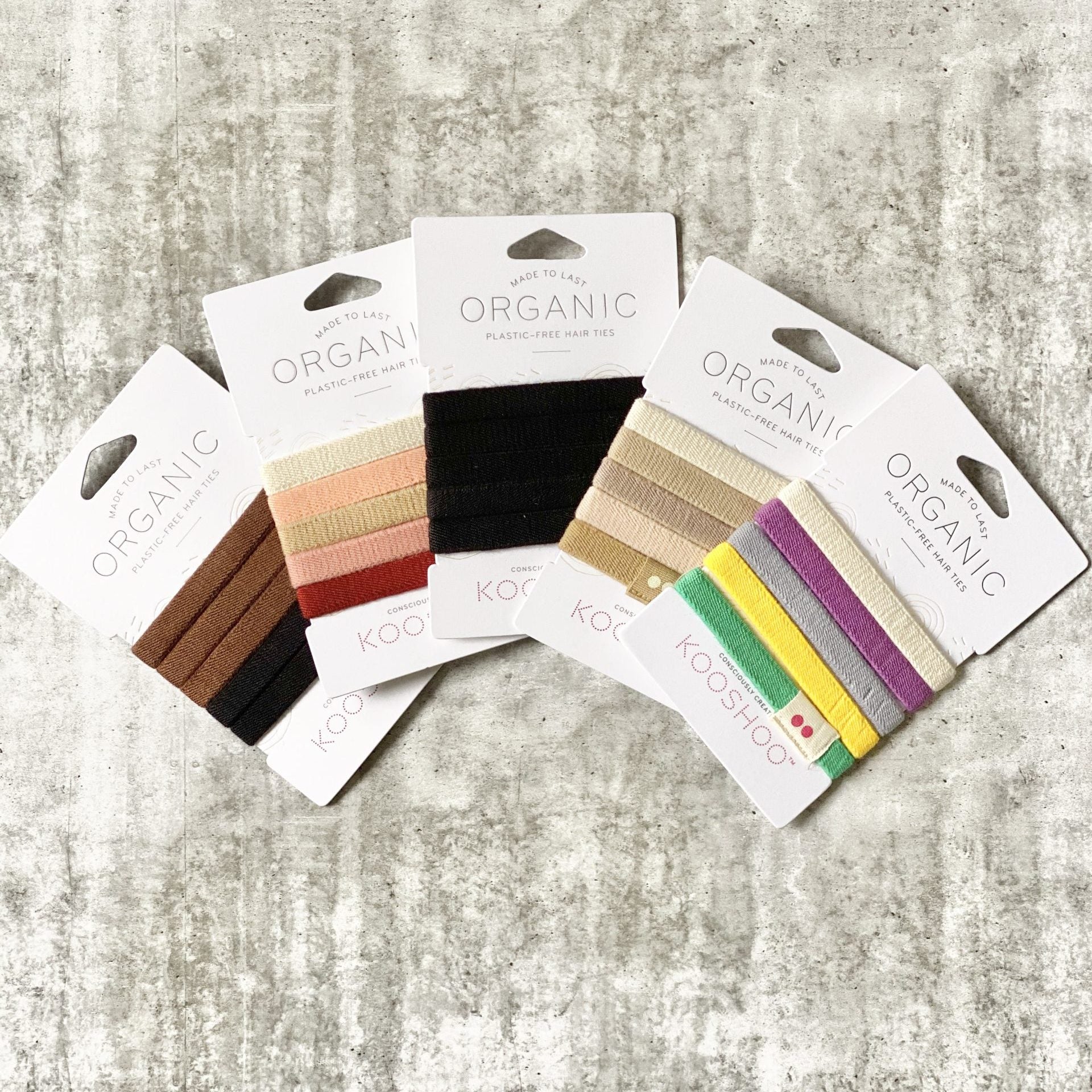 Set of Kooshoo organic hair ties in various colors on a textured gray surface