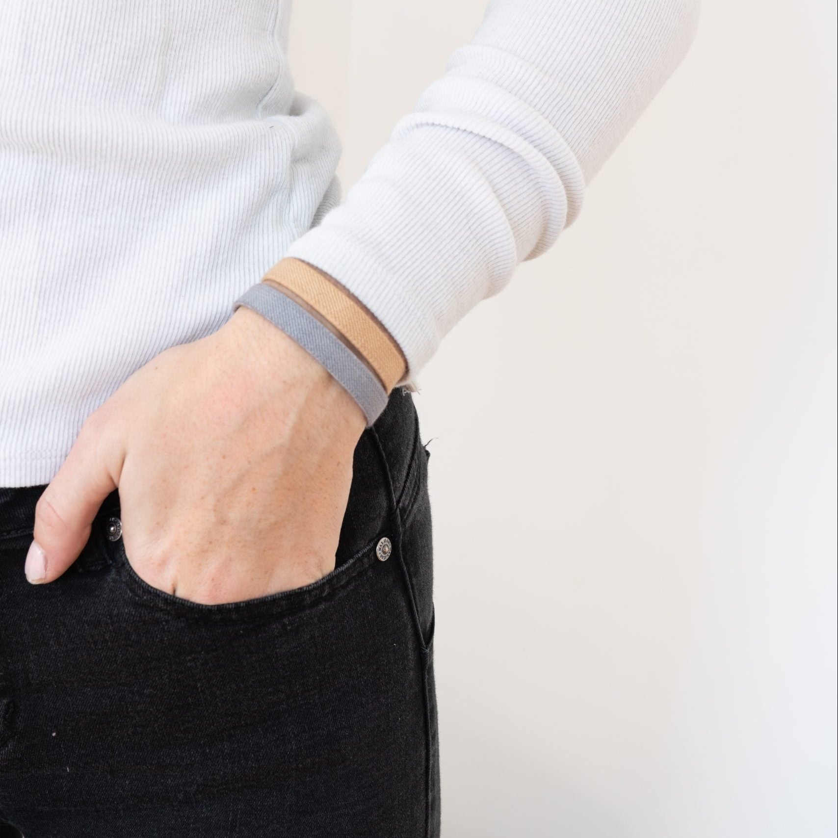 Person wearing a gray and blond Kooshoo organic hair tie on their wrist on a plain background