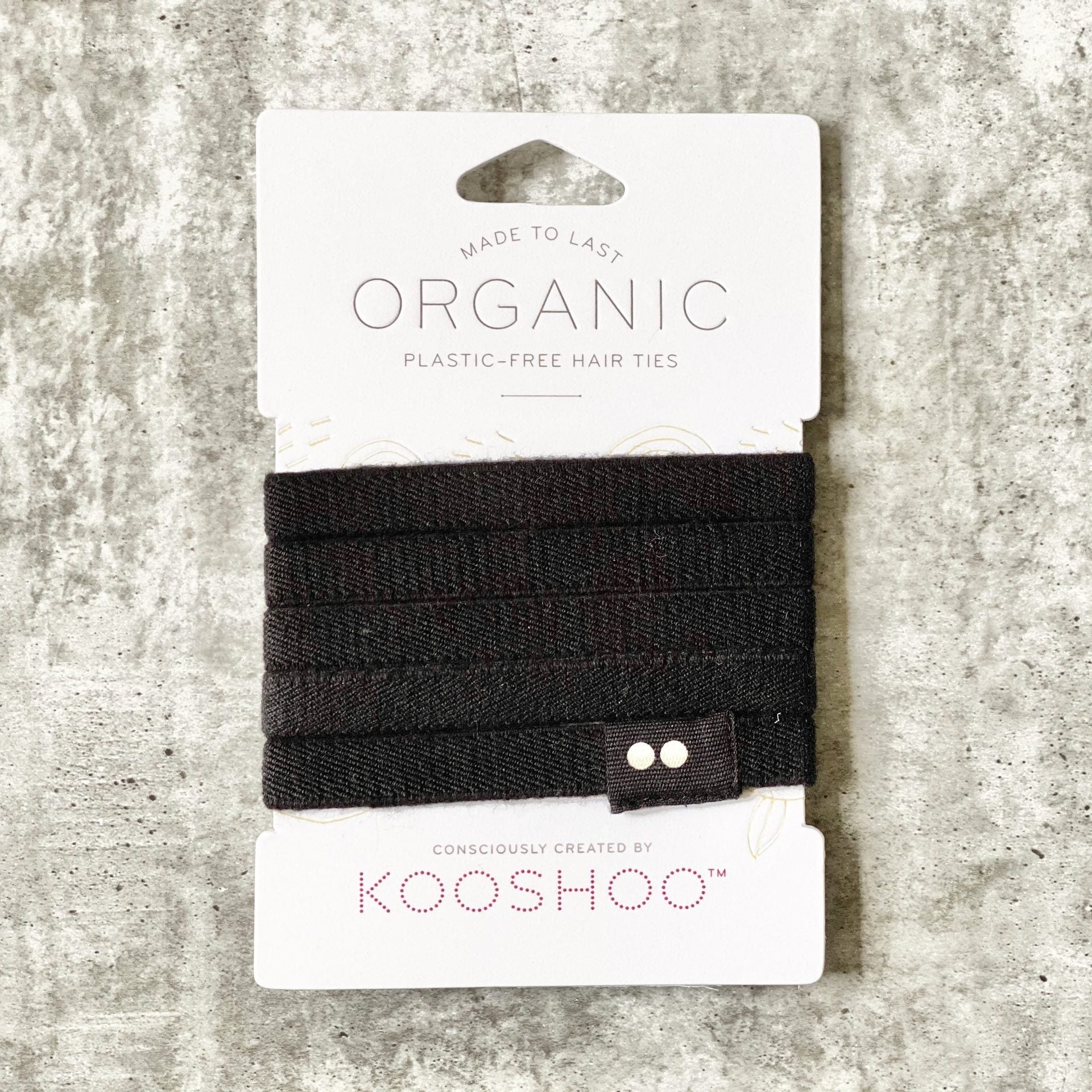 Set of Kooshoo organic plastic-free hair ties in black, against a textured gray background