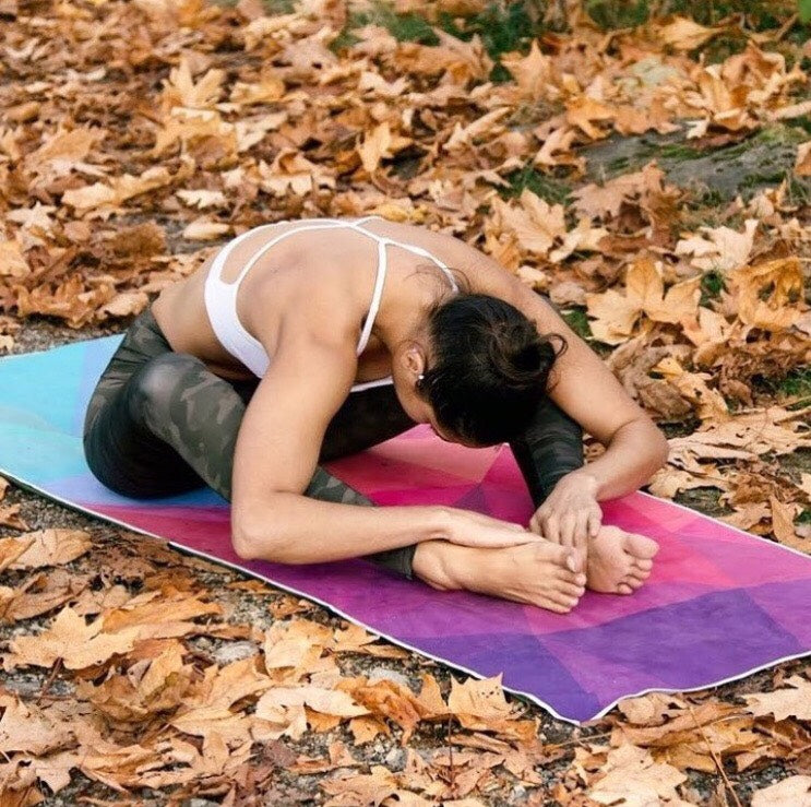 Person stretching on a colorful Yoga Design Lab yoga mat towel in an autumn setting with fallen leaves.