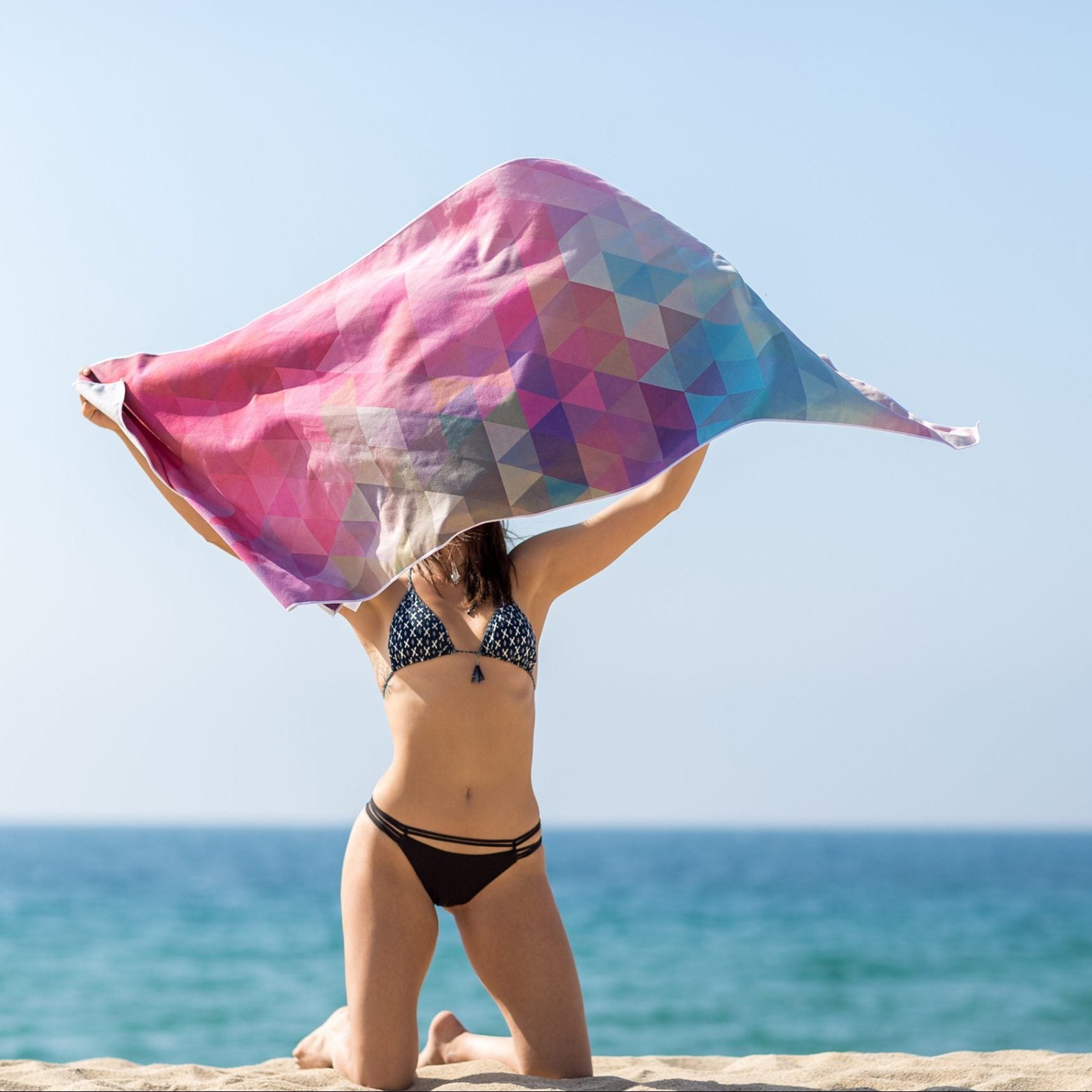 Woman holding a colourful Yoga Design Lab yoga towel by the ocean