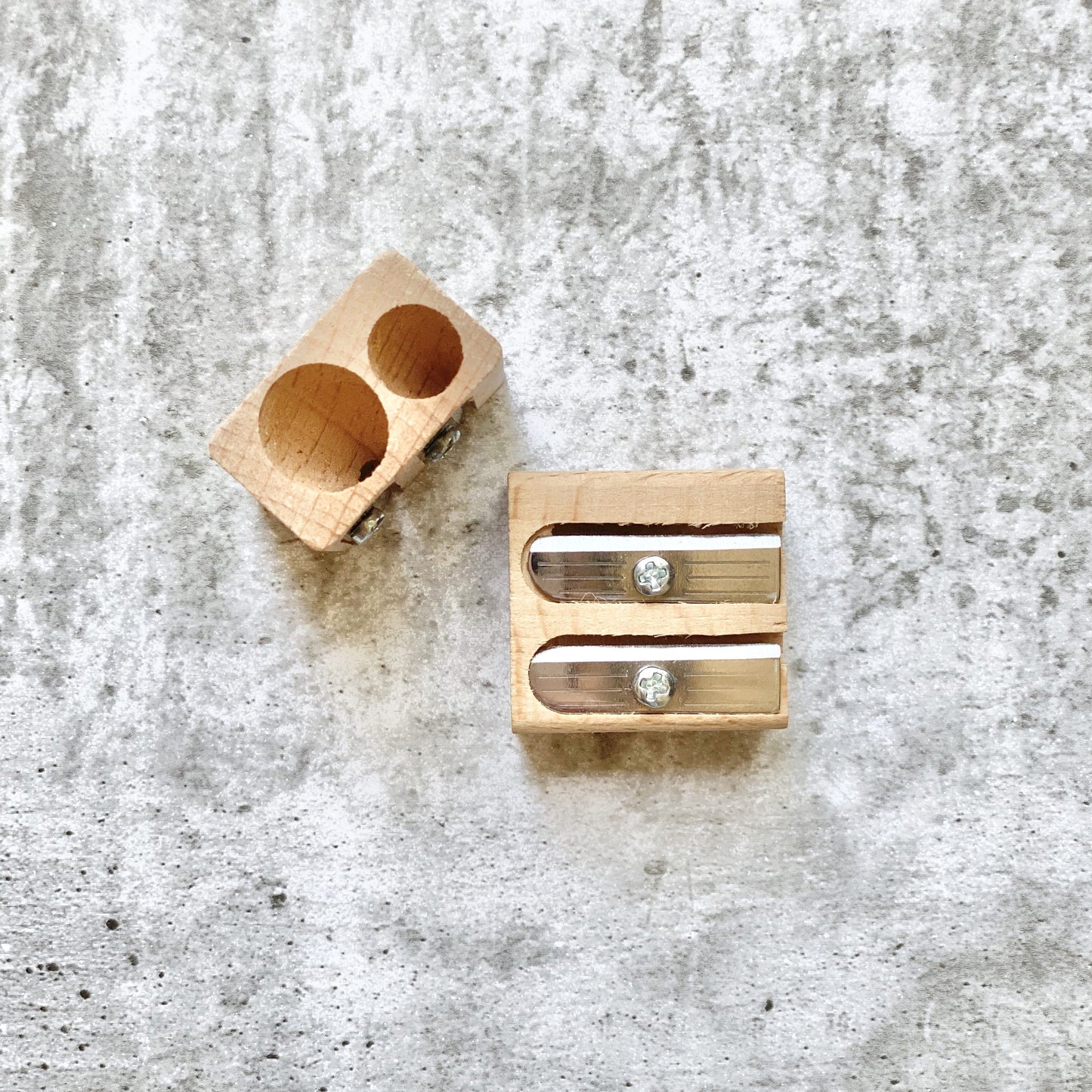 Earth Greetings wooden pencil sharpener with two cylindrical holes on a textured gray surface