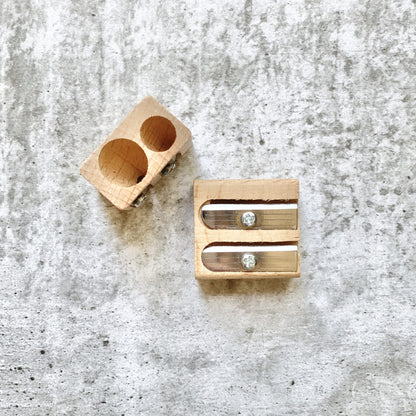 Earth Greetings wooden pencil sharpener with two cylindrical holes on a textured gray surface