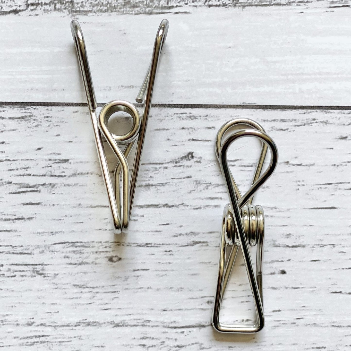 Two Ever Eco stainless steel clothes pegs on a white wooden surface