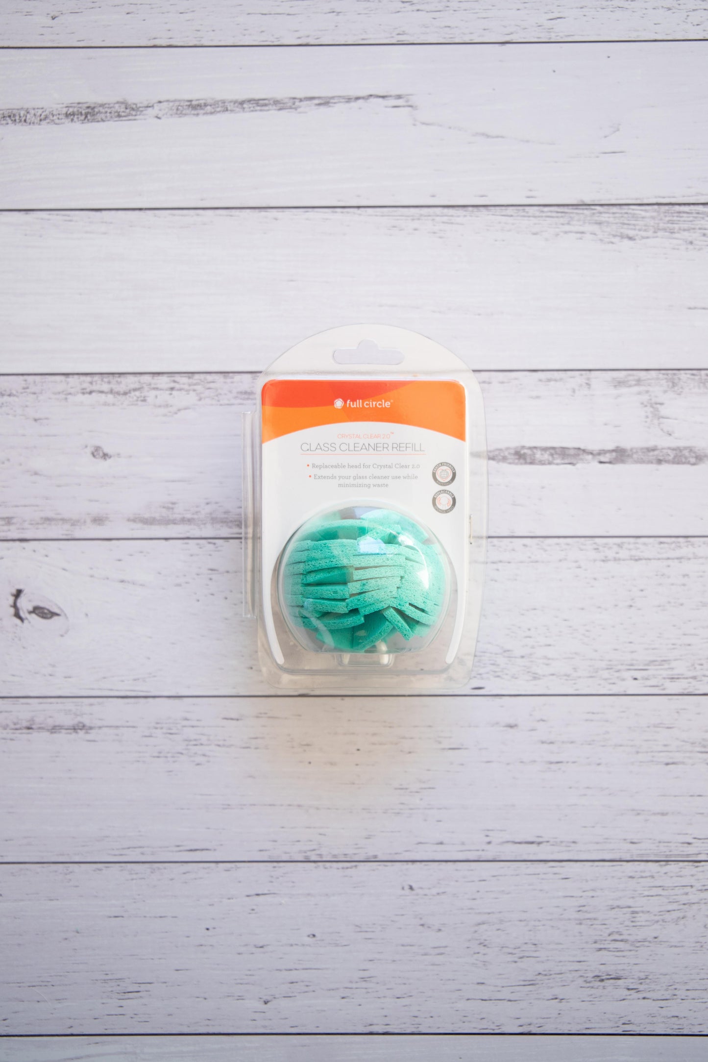 Full Circle turquoise cellulose glass cleaner ball with packaging on a light wooden surface