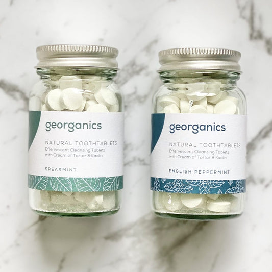 Two jars of Georganics natural tooth tablets in spearmint and English peppermint on a marble surface