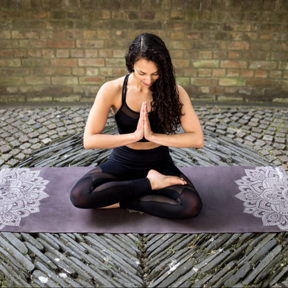 Woman practicing yoga on a black Yoga Design Lab combo mat with mandala pattern, with a brick wall background